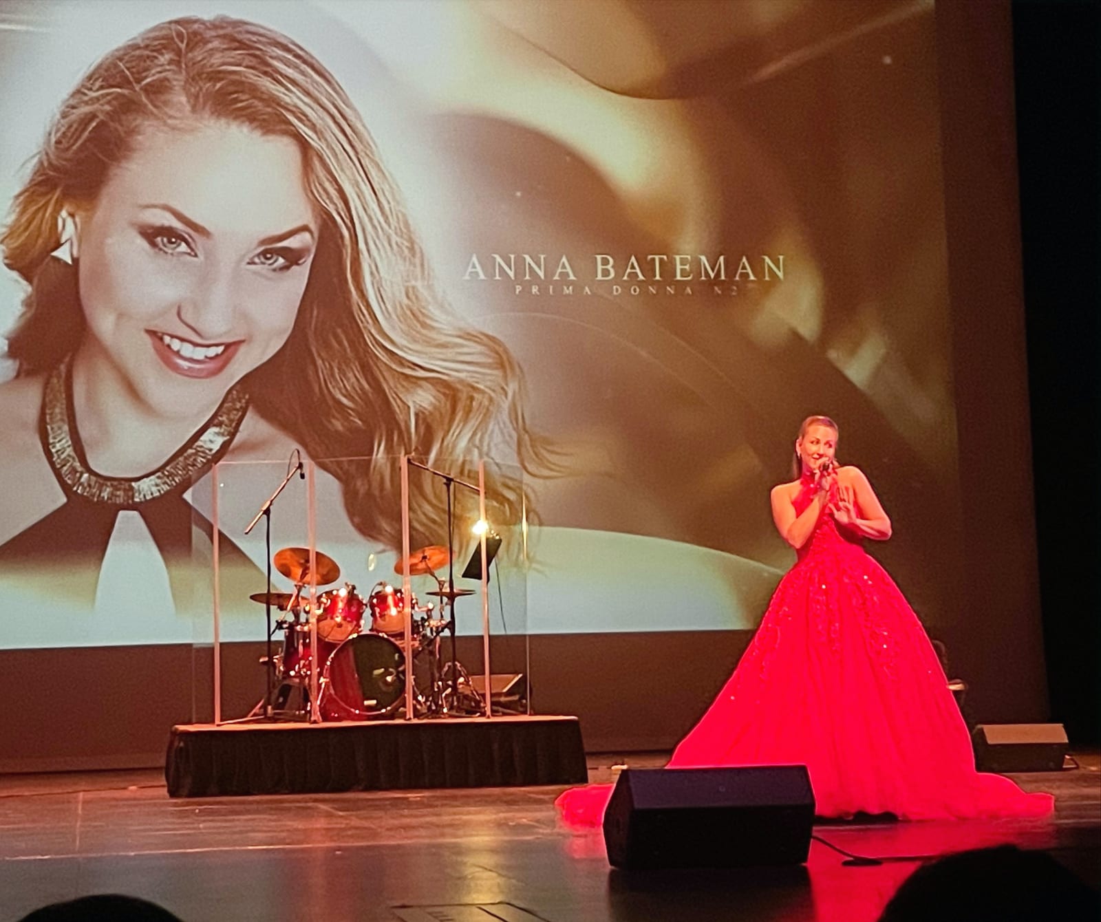 Anna Bateman performing in a red gown, her portrait projected behind her